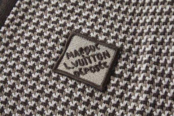 The jacket is brown and beige with a houndstooth-like pattern across the main body, and has solid, dark brown sleeves with a different knit texture