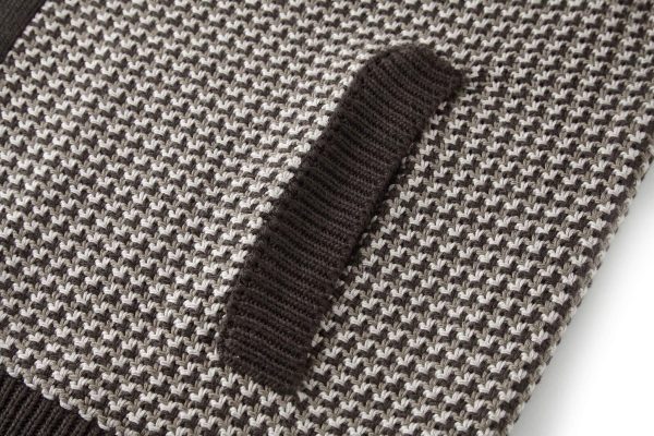 The jacket is brown and beige with a houndstooth-like pattern across the main body, and has solid, dark brown sleeves with a different knit texture