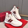 A pair of Bally Striped Leather Runner Sneakers in white and cream featuring burgundy side stripes and woven pull tabs, resting atop a red branded Bally shoebox.